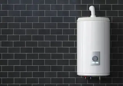 A modern white cylindrical water heater with a digital display is mounted on a dark tiled wall.