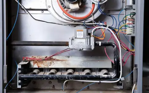 A view inside a furnace reveals rusted burners, a heat exchanger, and intricate wiring.