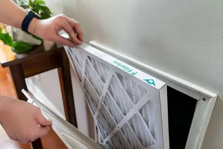 Hands insert a new 'Filterbuy' air filter, sized '16 x 25 x 1', into a wall return vent, demonstrating easy replacement.