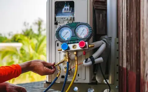 A technician connects a manifold gauge to an outdoor air conditioning unit.