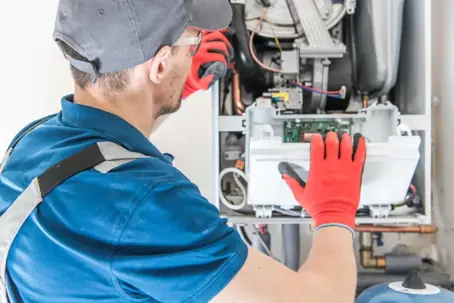 A technician in work gloves inspects the internal components of a gas boiler or water heater, actively troubleshooting the unit's intricate parts.