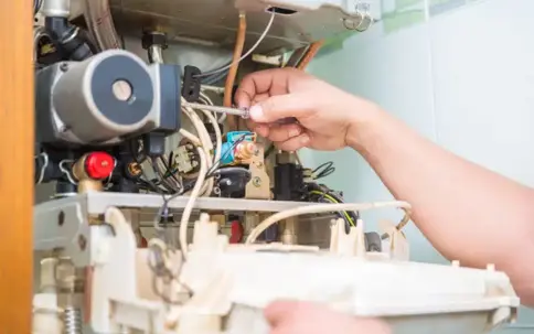 A person's hands work to repair the internal wiring and components of a heating unit