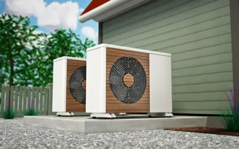 Two modern outdoor HVAC units with wood-look panels and fan grilles sit on a concrete slab next to a house.