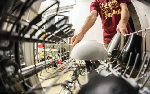 A fisheye view inside a dishwasher shows a person loading dishes.