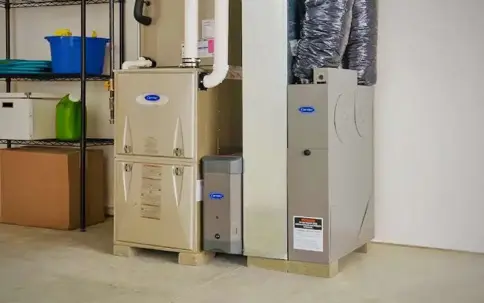 A utility room features two Carrier HVAC units; one tan with an attached humidifier, and a gray unit displaying a "DANGER: HIGH VOLTAGE" label.