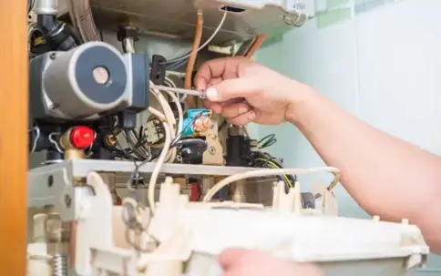 A person's hand using a screwdriver to service the complex internal components of a gas boiler or water heater.