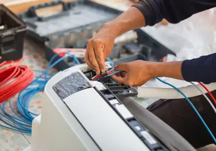 A technician's hands work on an indoor air conditioning unit