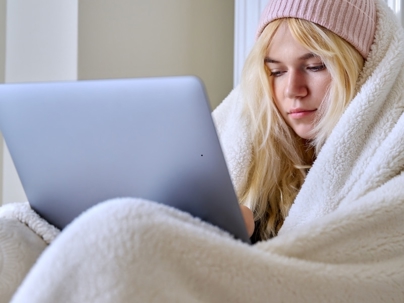 Girl wrapped up in blanket and looking at laptop on her lap