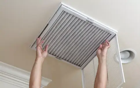 Hands install a clean 20x20x1 air filter into a ceiling return vent.