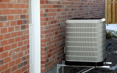 An outdoor air conditioning unit sits next to a red brick house wall