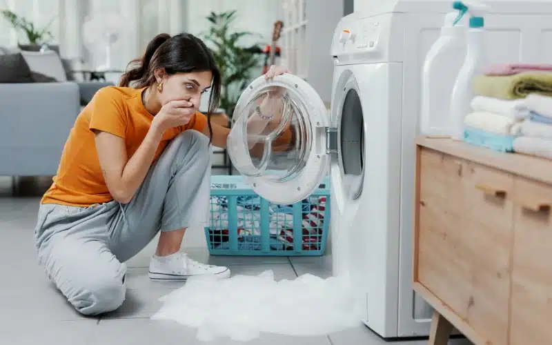 A woman reacts to a foul smell and leaking suds from her washing machine.