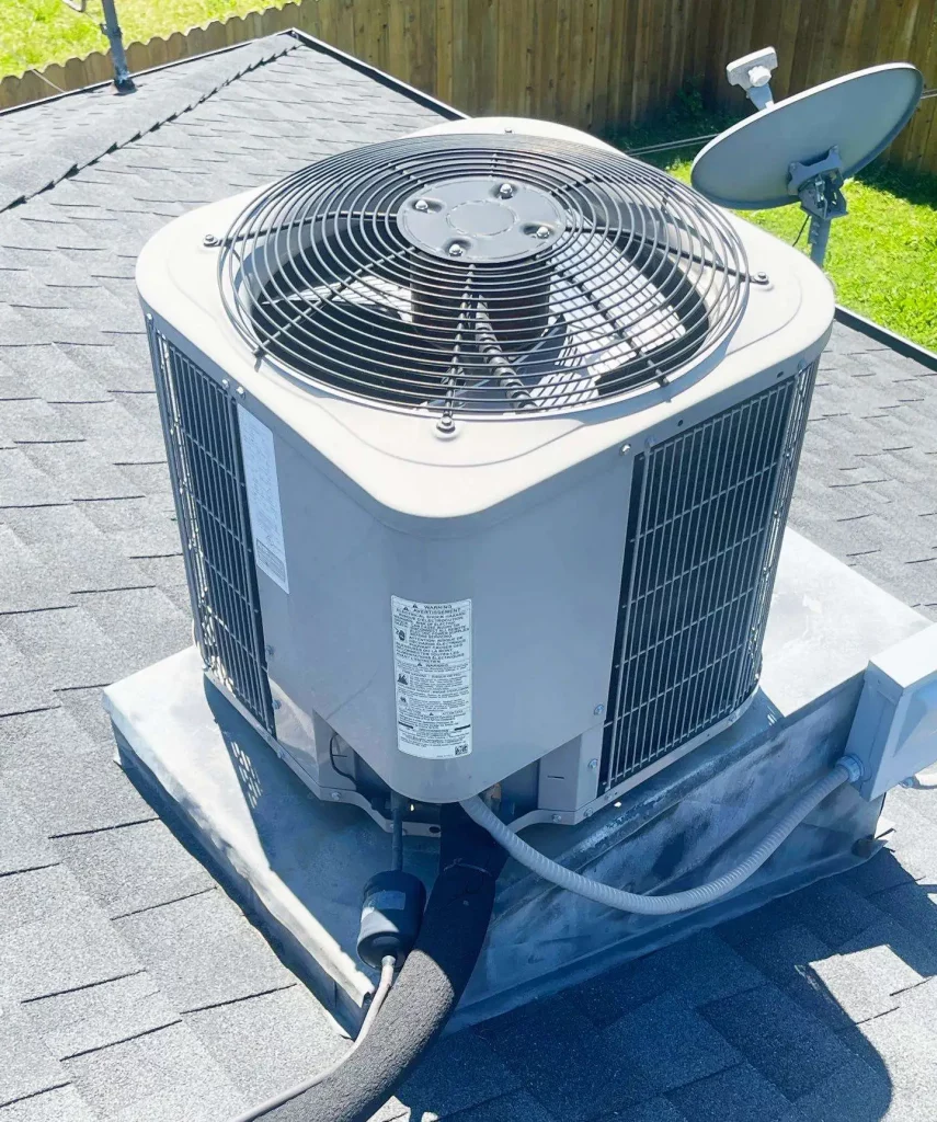 A modern AC condenser unit is installed on a shingled roof, perfect for spring setup. Important product labels are visible on its side.