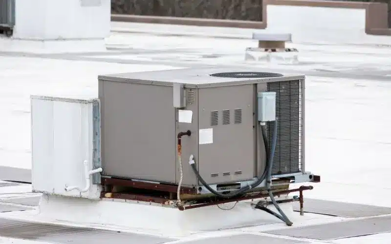 A large, gray commercial HVAC unit rests on a white rooftop, illustrating typical heating and cooling equipment.