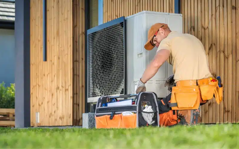 A skilled HVAC technician inspects an outdoor unit beside a modern home, with tools at the ready.