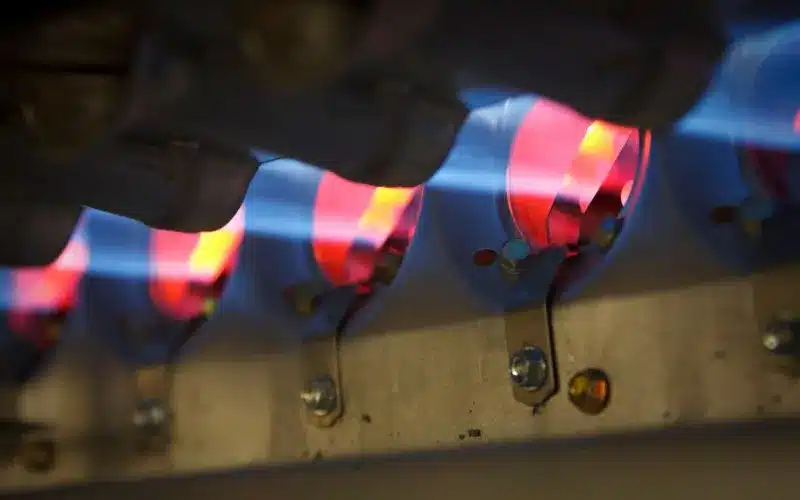 A close-up of a furnace igniter with blue flames heating red elements