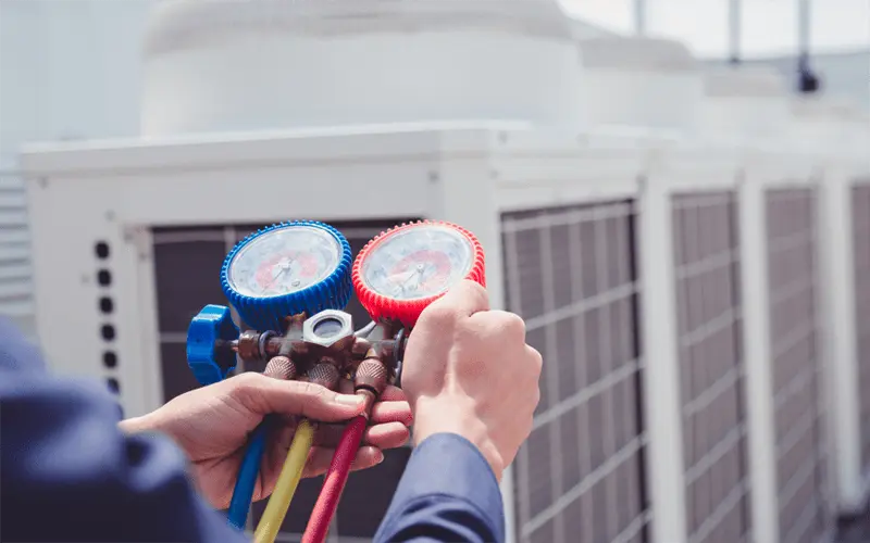 A technician uses a manifold gauge set, checking the pressure of an AC system.