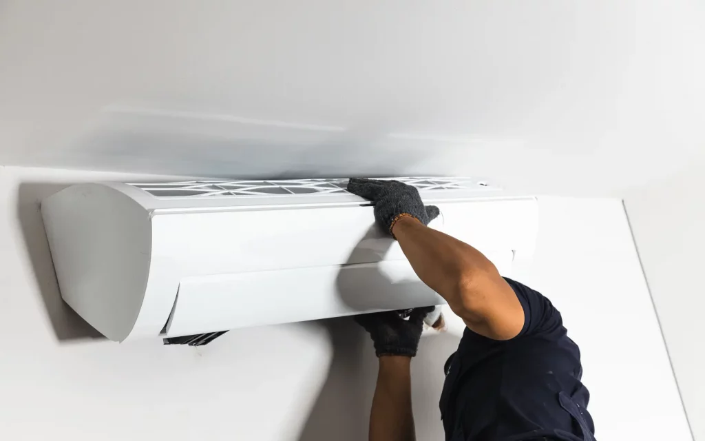 A worker installs a white indoor air conditioning unit on a white wall.