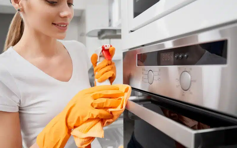 Wipes down a modern oven with a spray and cloth, embodying diligent oven care.