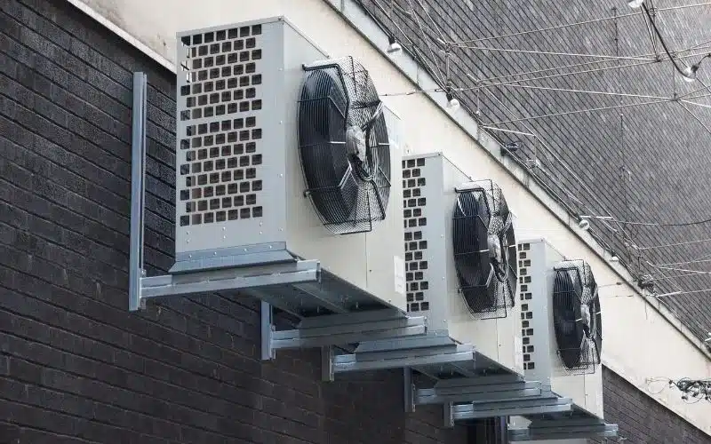 Four outdoor HVAC condenser units are professionally mounted on a dark brick wall.